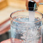 Closeup shot of a man pouring a glass of fresh water from a kitchen faucet