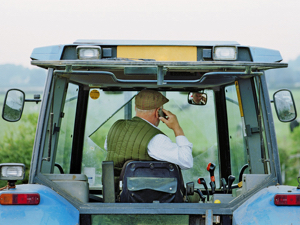 Senior male farmer driving tractor, using mobile phone, rear view