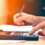 Close up young woman with calculator counting making notes at home, hand is writes in a notebook. Savings, finances, concept.