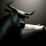 A closeup of two metal castings depicting a stylized bull alongside a bear in dramatic light representing financial market trends on an isolated dark background