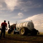 Farmer walks toward an air seeder with a blue sky above.