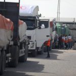 People gather around a line of flatbed trucks carrying humanitarian aid.