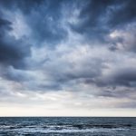 Dramatic stormy dark cloudy sky over sea, natural photo background