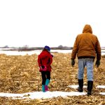 A farmer and a child walk in a field.