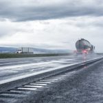 Semi truck drives down a wet highway with a cloudy sky overhead.