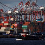 A tugboat passes shipping containers being unloaded and stacked on a pier at Port Newark, New Jersey, U.S., November 19, 2021.