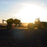 A tractor and seeder backlit by the spring sun.