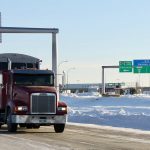 Semi truck drives near the Canadian border on a snowy day.