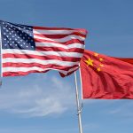 American and Chinese flags flying on a backdrop of blue sky.