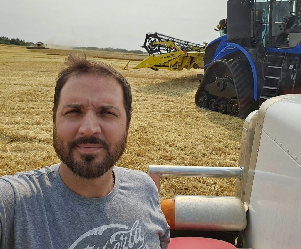 Damien C. Kurek poses with a tractor in a field at harvest.