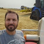 Damien C. Kurek poses with a tractor in a field at harvest.