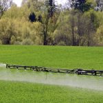 a sprayer unit spraying herbicide on a green crop