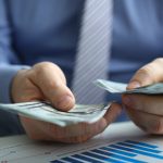 Male arm count hundred dollar bills closeup.