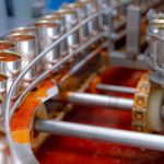 Canned fish factory. Food industry.  Sardines in red tomato sauce in tinned cans at food factory. Food processing production line. Food manufacturing industry. Many can of sardines on a conveyor belt.