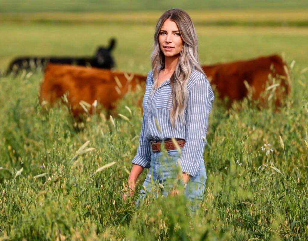 a young woman standing in a pasture with cows grazing in the background