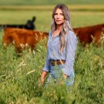 a young woman standing in a pasture with cows grazing in the background