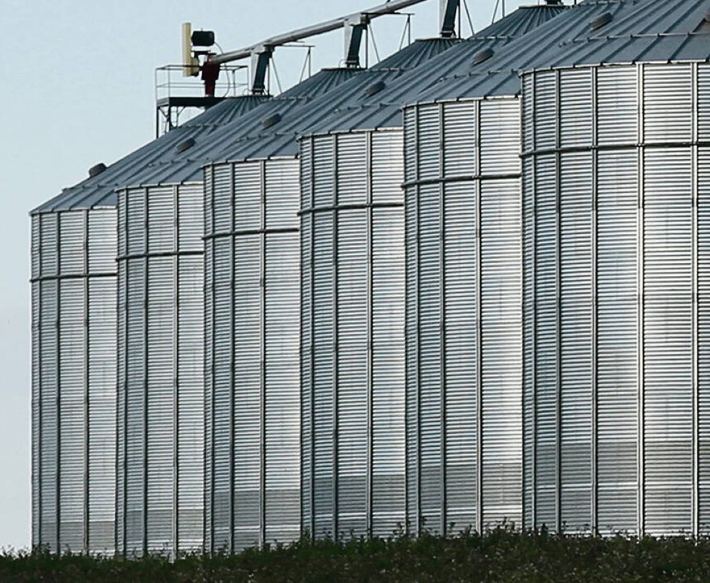 A row of six large grain bins at a grain terminal.