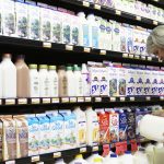 A woman bends down to read a label on a jug of milk in a milk cooler at a grocery store.