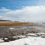 Melt water and melting snow in a harvested grain field in early spring. Rain storm in the background. Image taken in the afternoon in early spring.