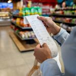 A person stands in a grocery story holding a long receipt. Photo: Hispanolistic/IStock/Getty Images