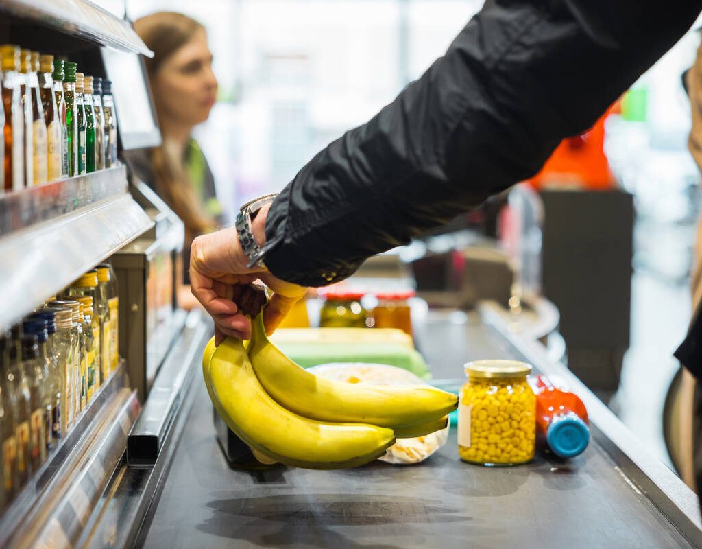 A person putting some bananas and other groceries on the conveyor at a store checkout. Photo: Getty Images