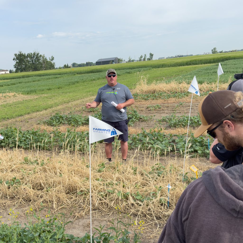 Ken Coles (centre) leads farmers and agronomists at the 2025 Farming Smarter Field School through research plots of an inter-row canola study while he presents on the impact of the various cover crop seeding rates and termination methods used in the trials.