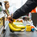A person putting some bananas and other groceries on the conveyor at a store checkout. Photo: Getty Images Plus