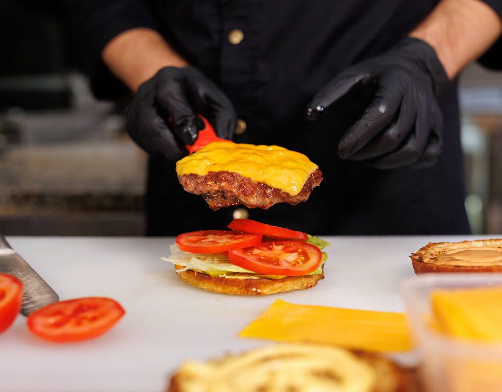 The cook in the kitchen prepares a cheeseburger and puts a cutlet with melted cheese. Photo: Artem Zakharov/Getty Images Plus