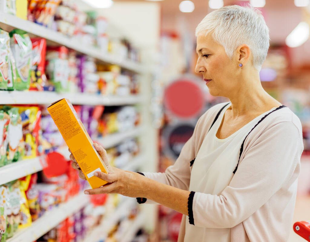 A woman stands in a grocery store reading the label on a cereal box. Photo: vgajic/Getty Images Plus