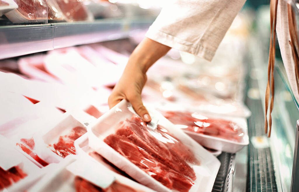 A hand reaches to pick up a package of meat at a grocery store meat cooler. Photo: Getty Images Plus