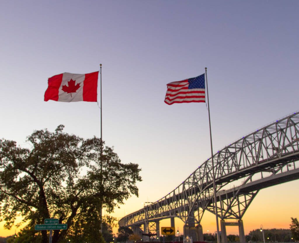 The Canadian and American flags fly next to each other against the sunset. Photo: ehrlif/istock/GettyImages