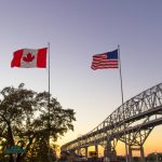 The Canadian and American flags fly next to each other against the sunset. Photo: ehrlif/istock/GettyImages