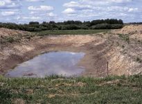 a low-water level dugout on a pasture during drought conditions