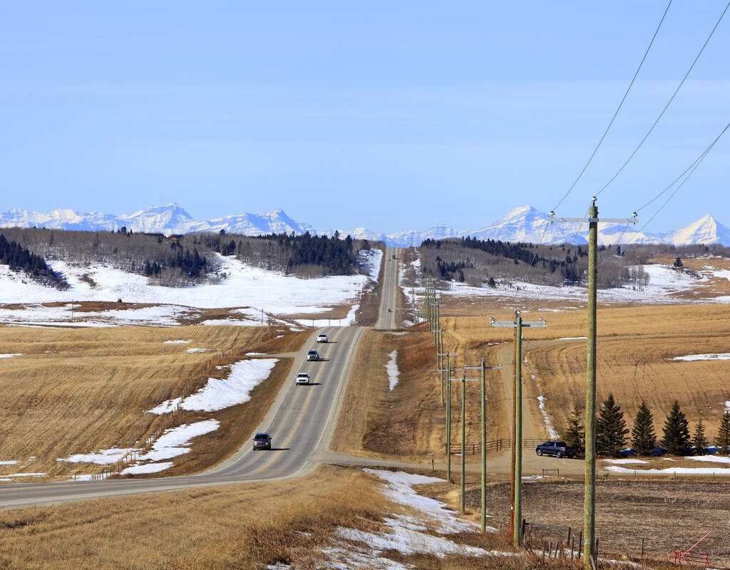 Alberta rural highway between Calgary and Cochrane looking west in early March. Snow covered Rocky Mountains in Distance. Photo: Getty Images Plus