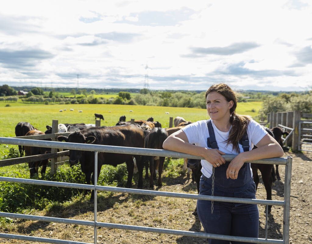 A three-quarter-length portrait shot of a mid-adult female farmer standing at her farm, she is looking away with a smile. Photo: Getty Images Plus