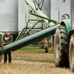 Young man working on farm operating grain auger alongside grain bins. Photo: AJ_Watt/Getty Images Plus