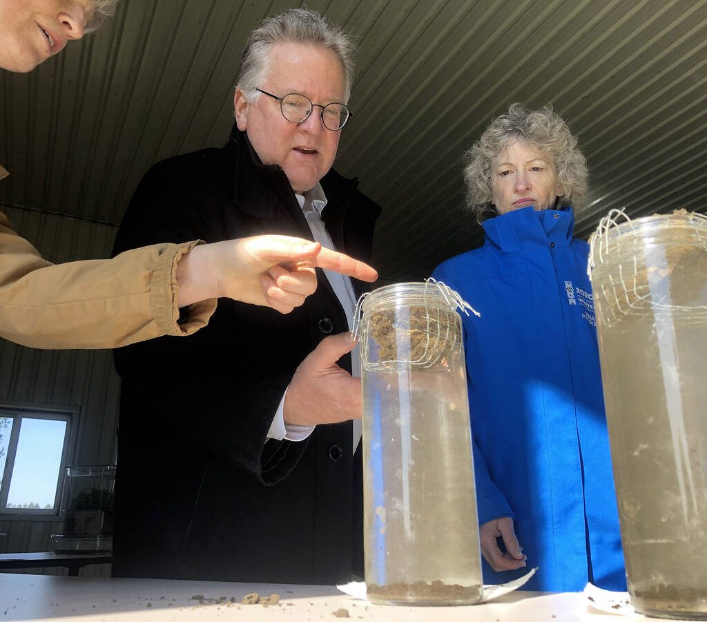 Under the direction of Heather White, Soils at Guelph, far left, Ontario Senator Rob Black, centre, and Yukon Senator Pat Duncan, right, compare the integrity of two soil samples gently laid mesh baskets to see which will hold their form and which will crumble in long tubes of still water.