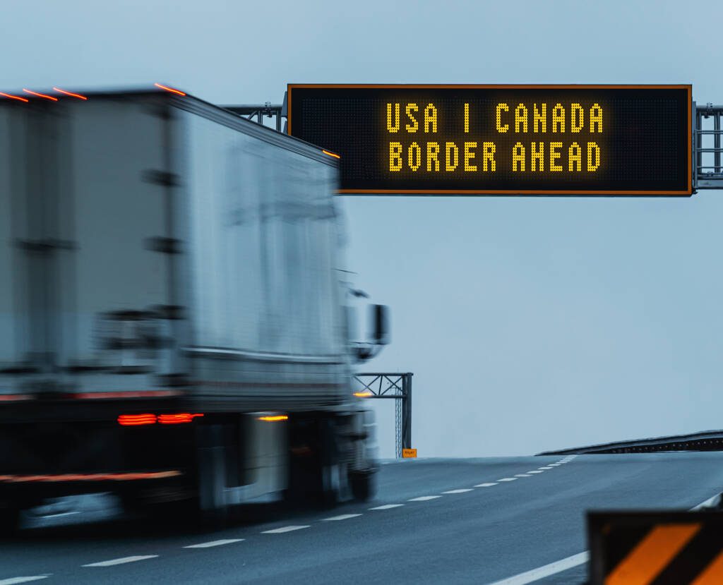 Semi truck approaching a border ahead highway sign.