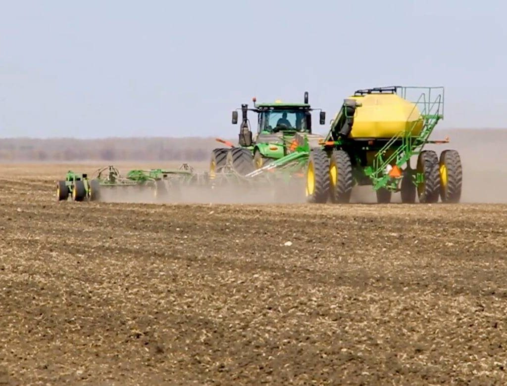A green tractor pulls a green and yellow air seeder through a cultivated field. Photo: Greg Berg