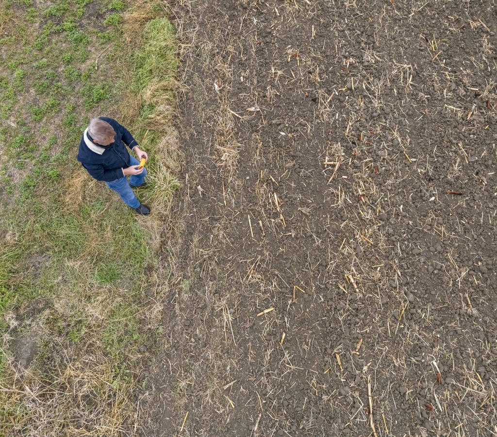 An overhead view of a farmer looking at a cultivated field that doesn't have anything much growing in it.