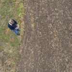 An overhead view of a farmer looking at a cultivated field that doesn't have anything much growing in it.