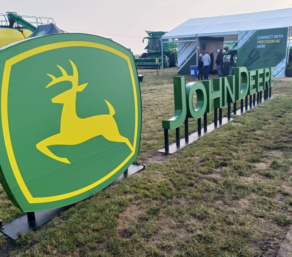 A John Deere logo stands in an outdoor, grassy area at a farm show.
