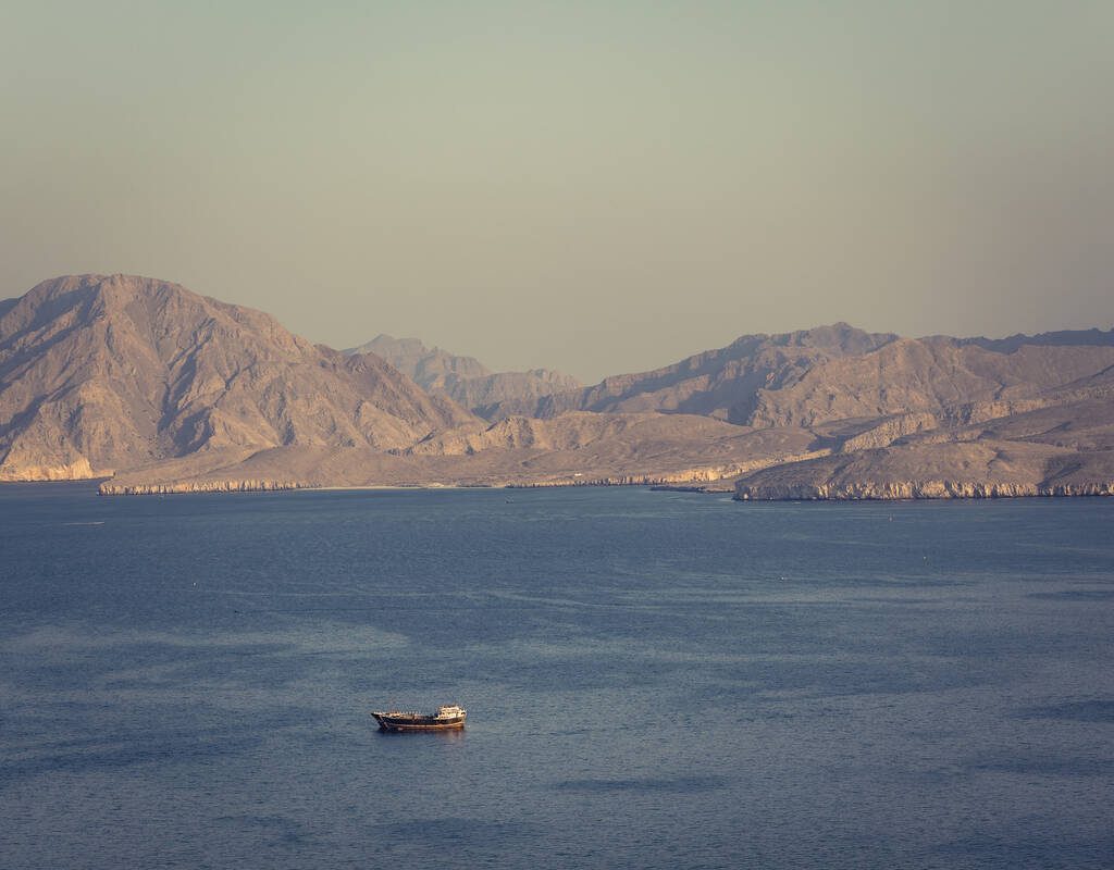 A view of the Strait of Hormuz with a small boat in the foreground and hills in the background.