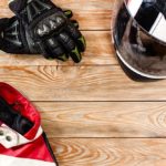 Overhead view of biker accessories placed on rustic wooden table. Items included motorcycle helmet, gloves and jacket. Motorcycle travel dream concept.